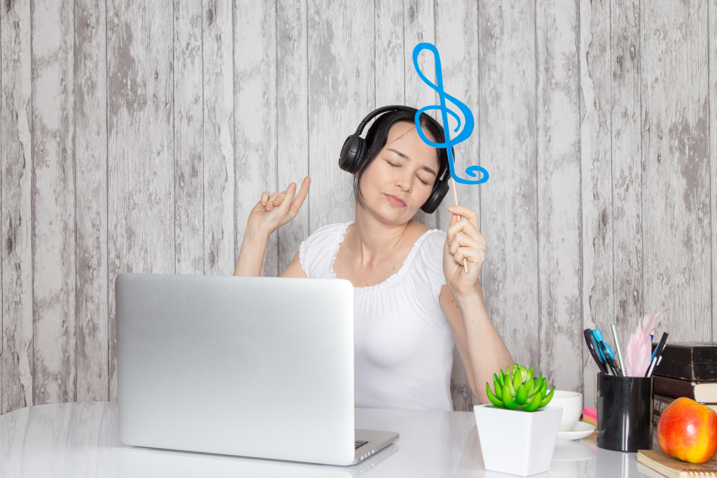 young-lady-white-shirt-holding-blue-note-listening-music-through-black-earphones-table-along-with-green-plant-pens-grey.jpg